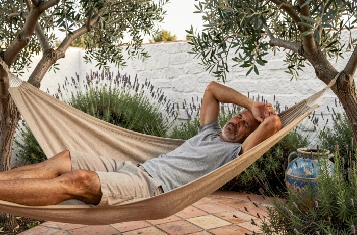 Homme allongé dans un hamac dans un jardin méditerranéen, illustrant le difficile repos lors d'un burn-out en vacances