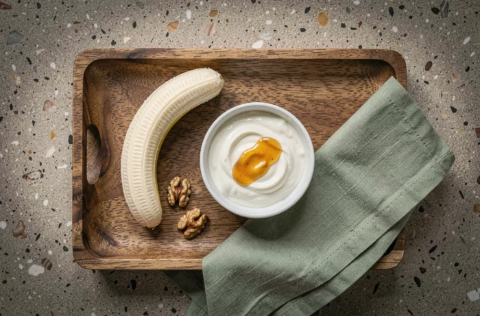 Plateau petit déjeuner vue du dessus avec banane coupée, yaourt grec, miel et noix sur comptoir en pierre